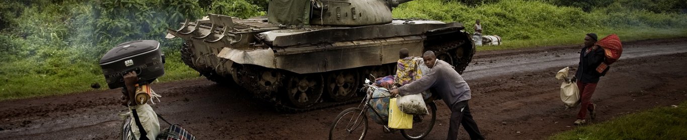 Un tank s'avance sur une route tandis que des personnes s'enfuient en sens inverse.  Kibumba, est du Congo. 