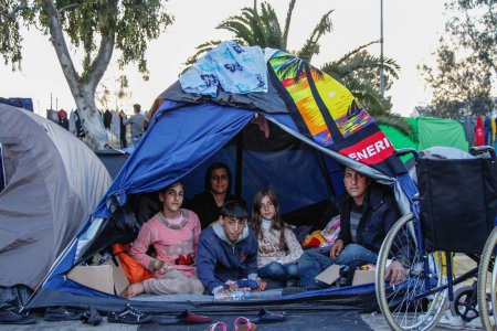 A man and his children are under a tent in Piraeus port in Athens